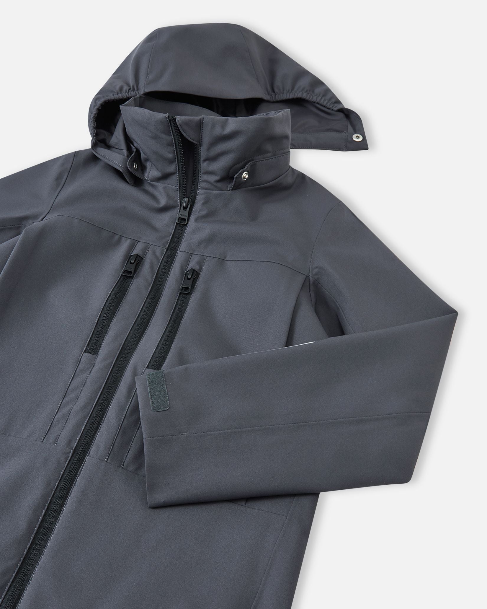 Close-up of the detachable, weather-protective hood and high collar on the soft black Reima Saarela kids waterproof jacket.