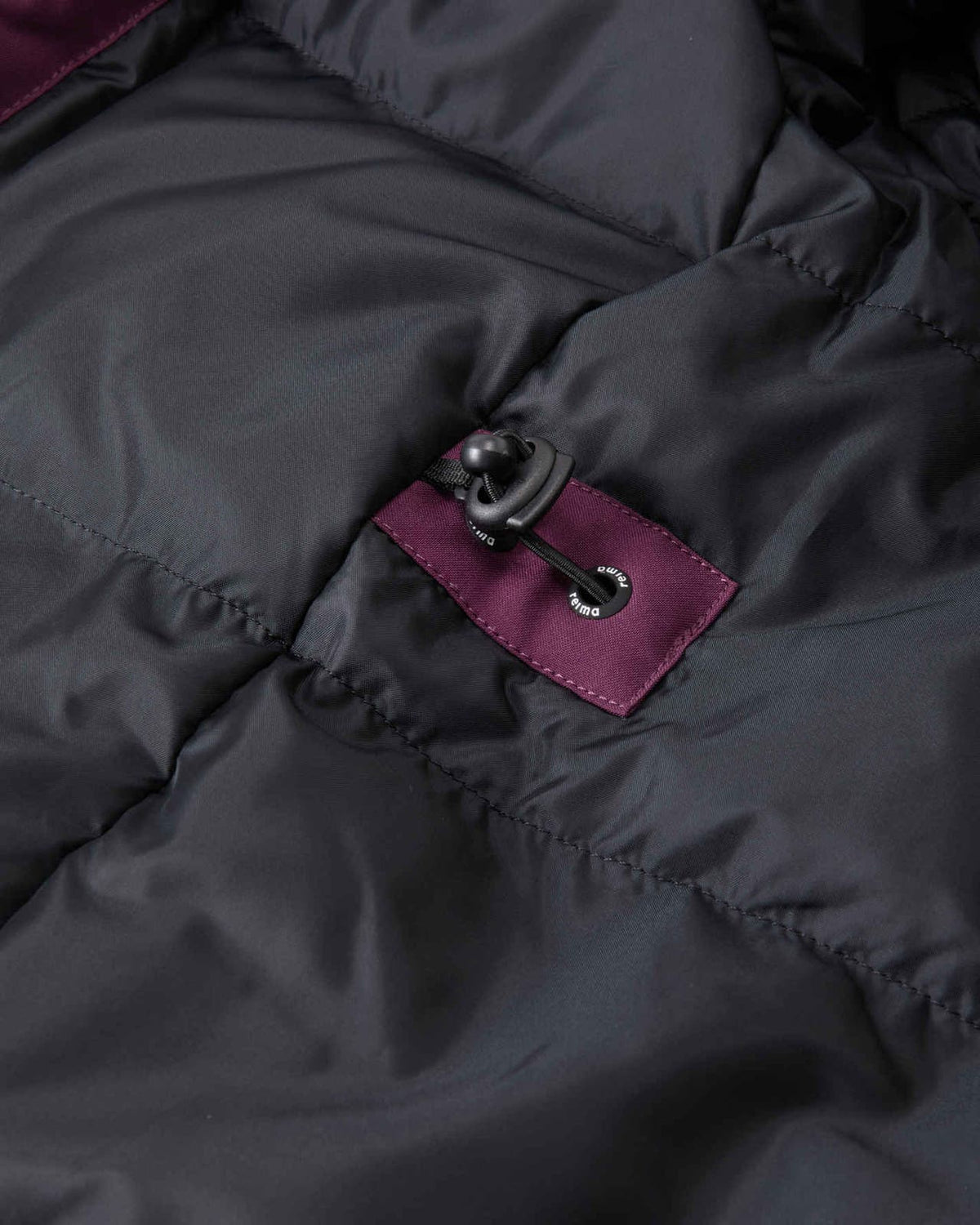 Close-up of the interior lining of the deep purple Reima Serkkula kids' parka, showing smooth black down baffles, a reinforced purple fabric patch, and an elastic waist adjustment toggle.