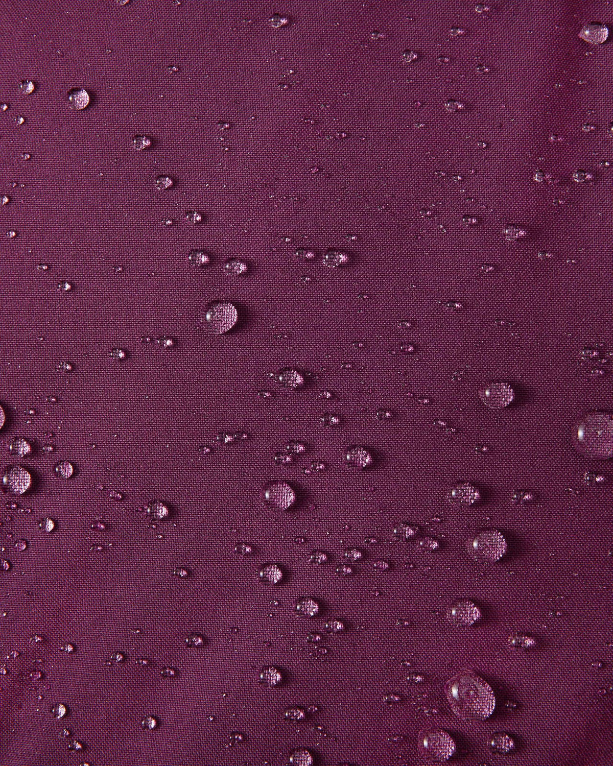 A macro close-up of the deep purple Reimatec fabric used on the Reima Serkkula kids' down parka, showing multiple water droplets beading on the surface to demonstrate its fully waterproof and water-repellent capabilities.