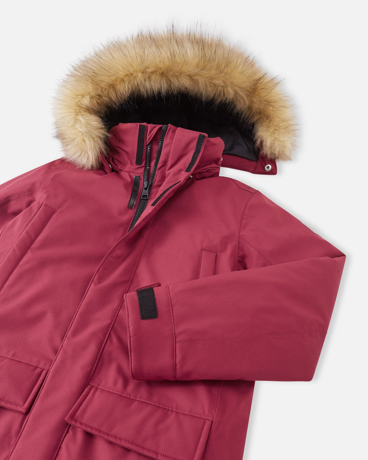 A close-up detail shot of the maroon Reima Serkkula kids' down parka, focusing on the collar, sleeve cuff area, durable fabric texture, and upper patch pocket.