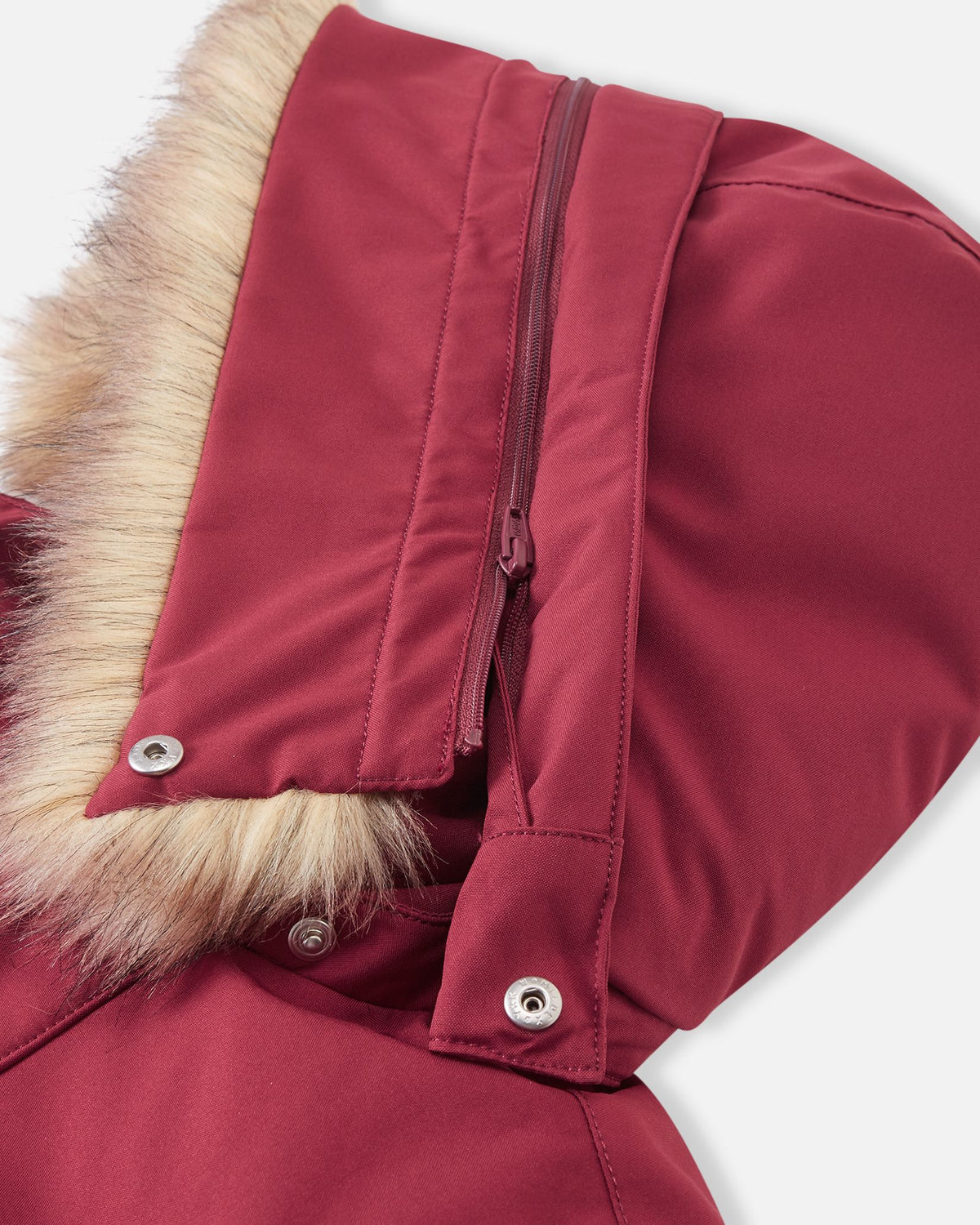 A detailed close-up of the hood detachment mechanism on the maroon Reima Serkkula kids' parka, showing the metallic snaps for securing the faux fur and the zipper connecting the hood to the collar.