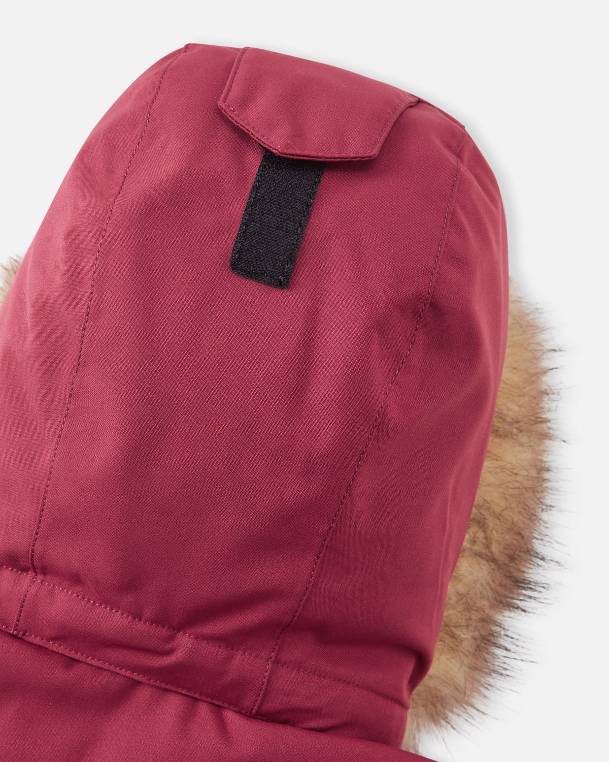 A detailed shot focusing on the crown of the hood on the maroon Reima Serkkula kids' parka, highlighting the Velcro adjustment tab used for customizing the fit.