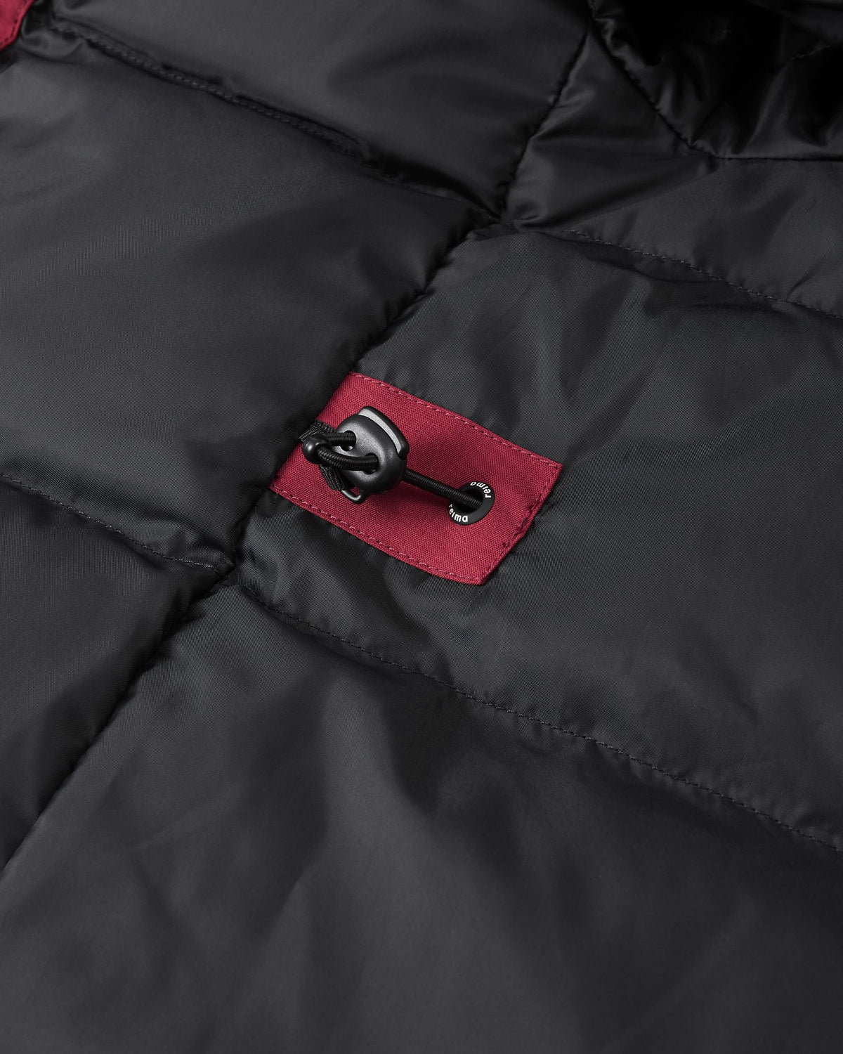 A close-up image of the interior of the maroon Reima Serkkula kids' parka, showing the black quilted inner lining with a maroon panel and a drawstring toggle for waist adjustment.