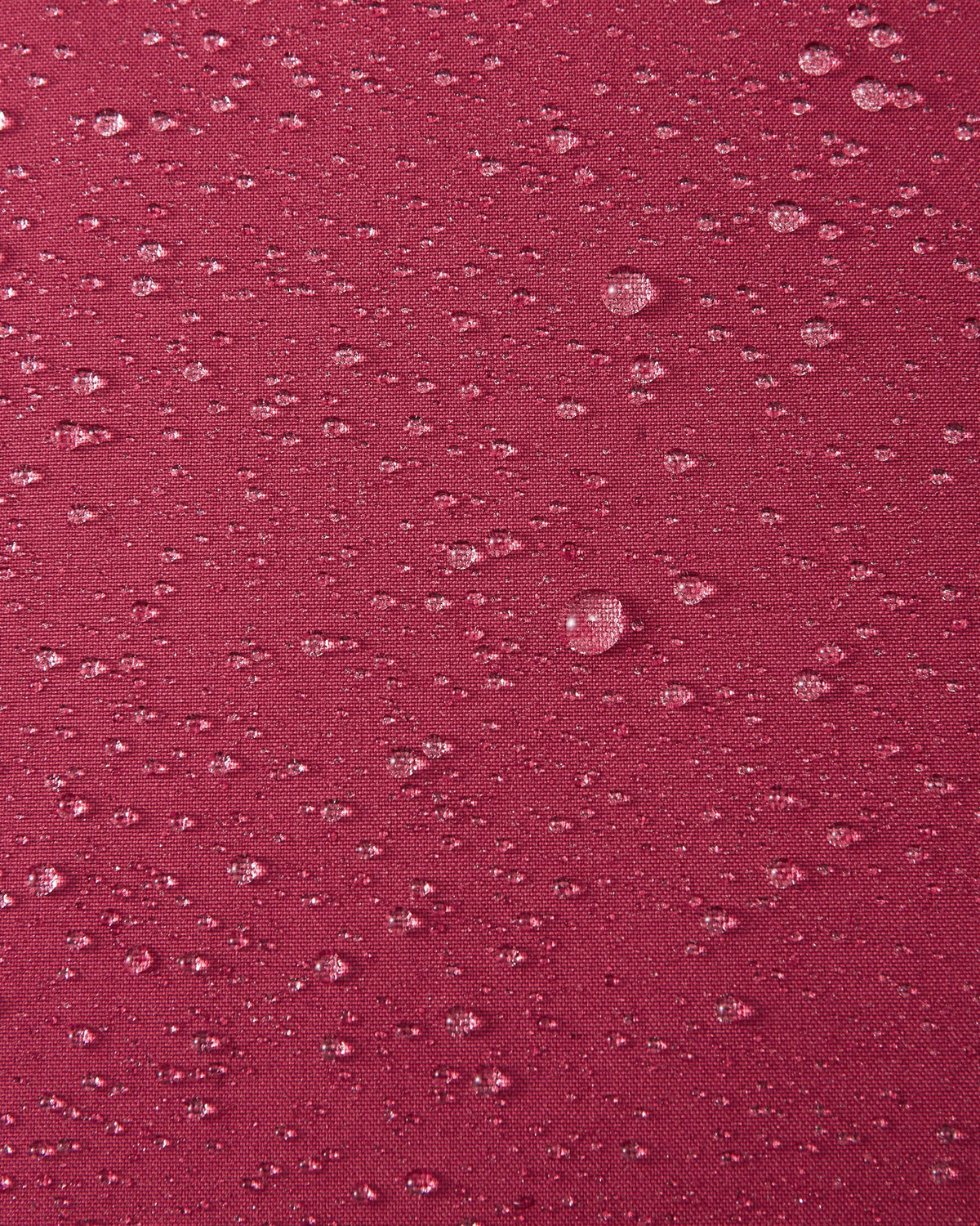 A macro close-up of the maroon Reimatec fabric used in the Reima Serkkula kids' down parka, showing multiple water droplets beading on the surface to demonstrate its fully waterproof and water-repellent capabilities.