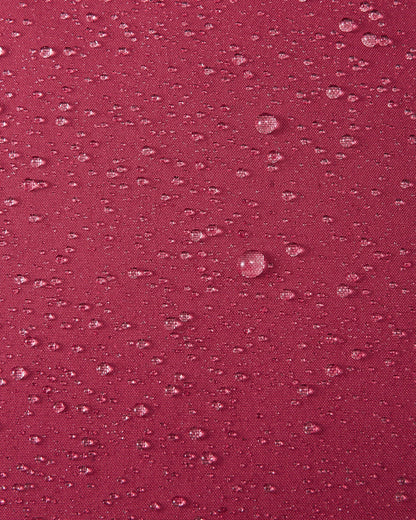 A macro close-up of the maroon Reimatec fabric used in the Reima Serkkula kids' down parka, showing multiple water droplets beading on the surface to demonstrate its fully waterproof and water-repellent capabilities.