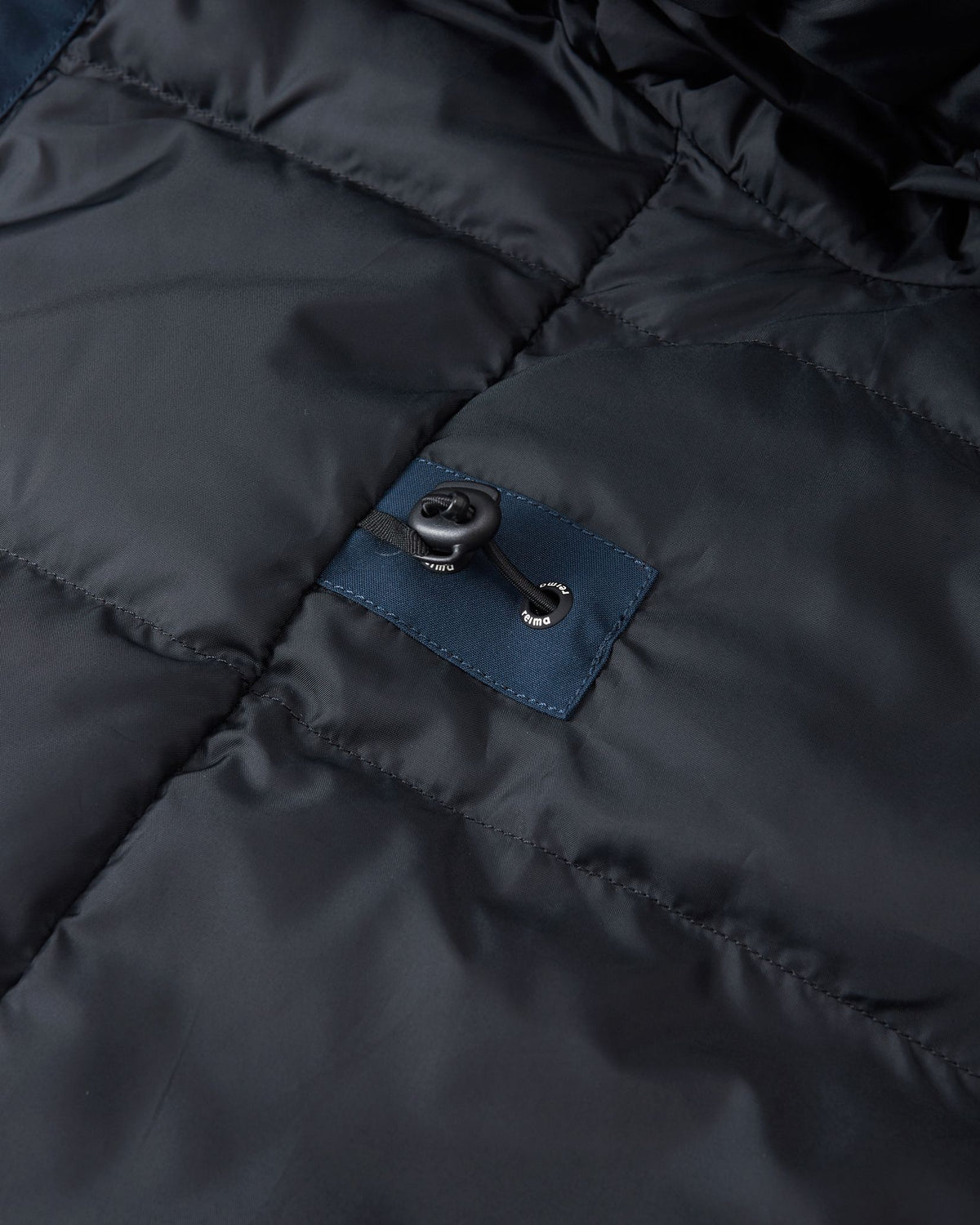 Interior detail of the navy Reima Serkkula parka, showing the smooth quilted lining and elastic waist-cinch drawstring toggle.