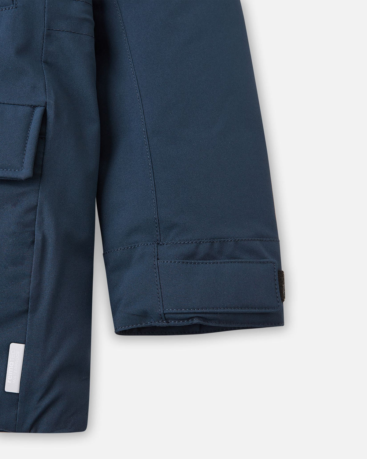 Close-up of the sleeve cuff with an adjustable Velcro strap, lower flap pocket, and sewn-in reflective safety tag on the navy Reima Serkkula parka.