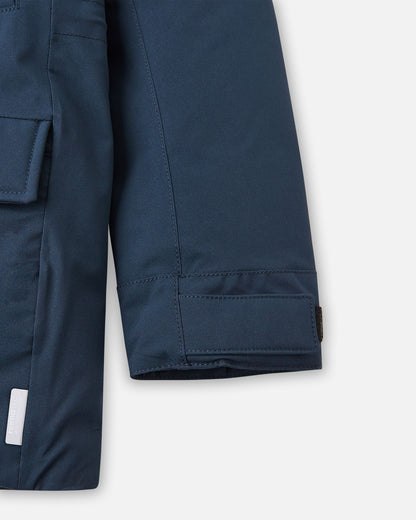 Close-up of the sleeve cuff with an adjustable Velcro strap, lower flap pocket, and sewn-in reflective safety tag on the navy Reima Serkkula parka.