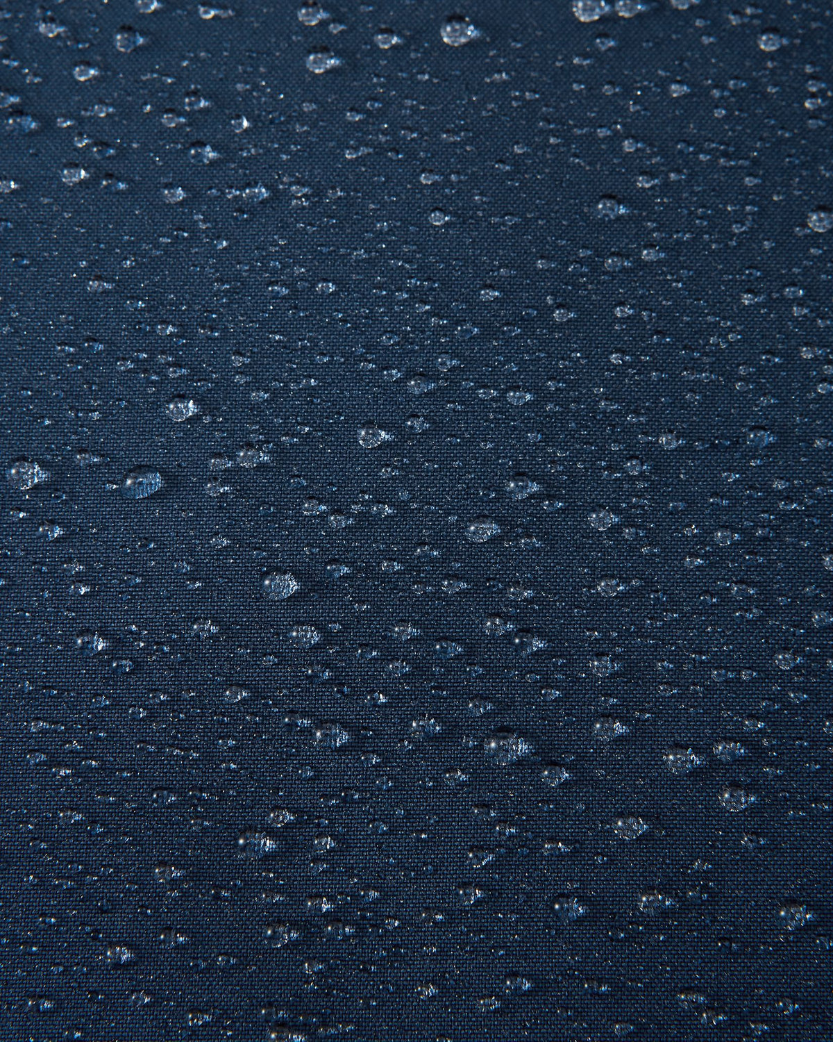 A macro close-up of the navy blue Reimatec fabric used on the Reima Serkkula kids' down parka, showing multiple water droplets beading on the surface to demonstrate its fully waterproof and water-repellent capabilities.