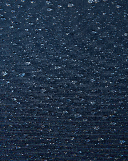 A macro close-up of the navy blue Reimatec fabric used on the Reima Serkkula kids' down parka, showing multiple water droplets beading on the surface to demonstrate its fully waterproof and water-repellent capabilities.