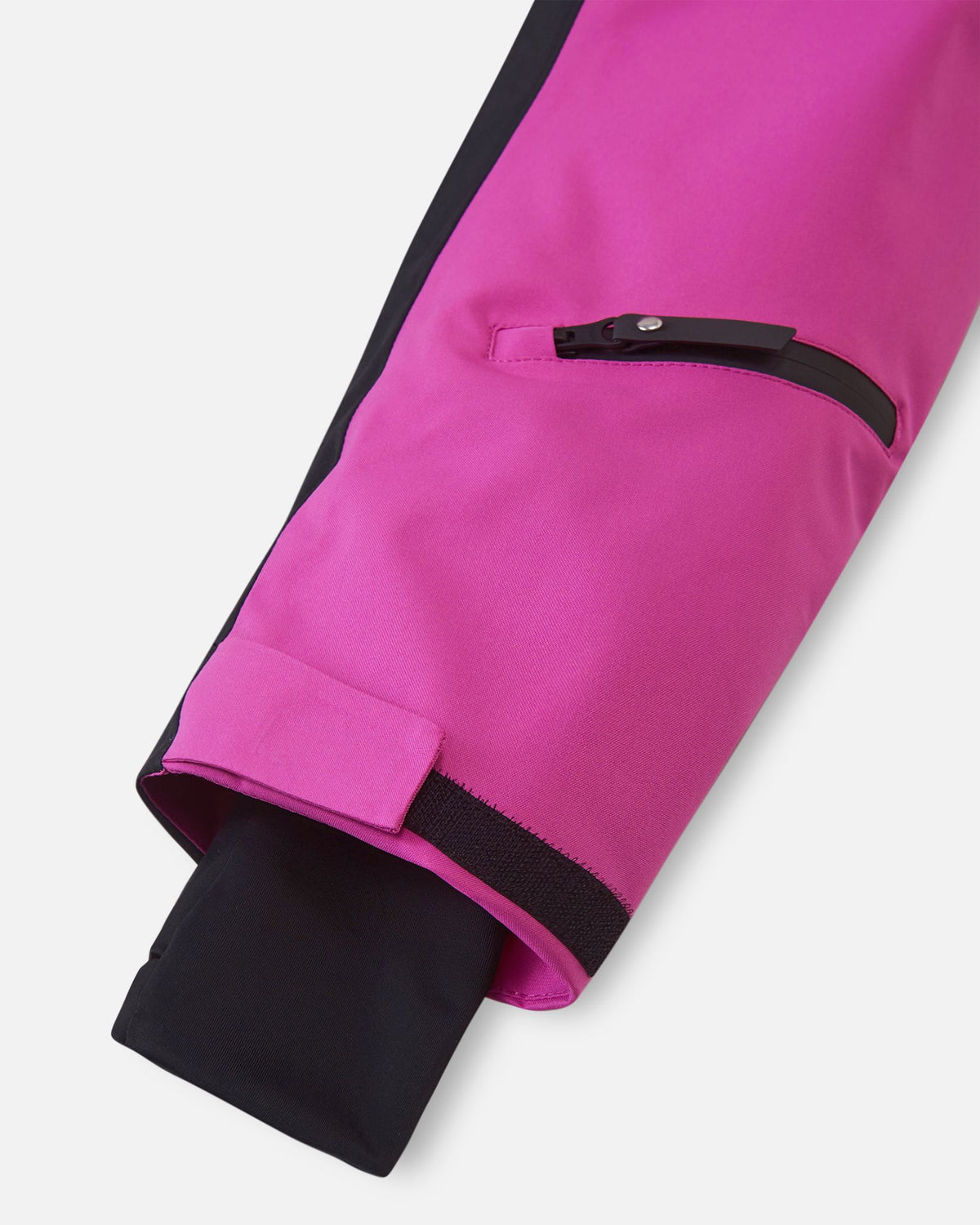 Close-up of the sleeve on the Reima Skaulo girls ski suit in fuchsia, featuring a small zippered pocket, an adjustable velcro cuff, and a comfortable inner lycra wrist gaiter.