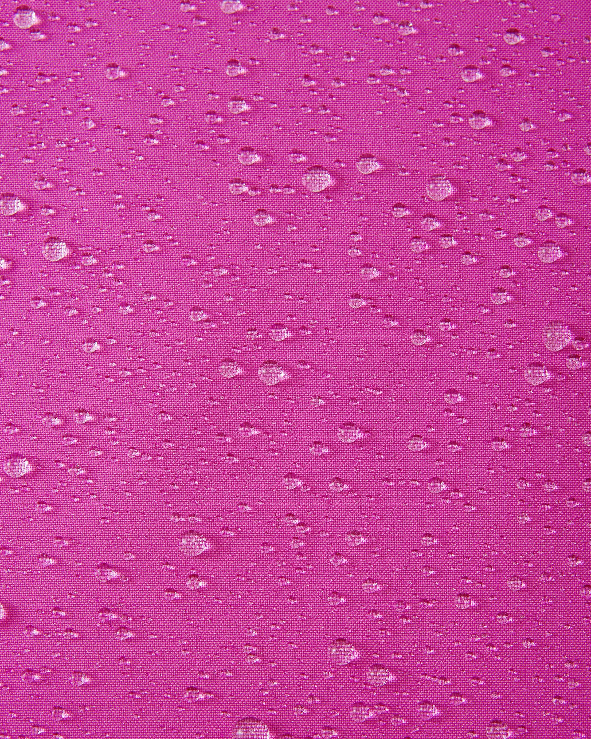 Macro detail shot of water droplets beading up on the bright fuchsia fabric of the Reima Skaulo girls ski suit, demonstrating its high-quality waterproof and dirt-repellent finish.