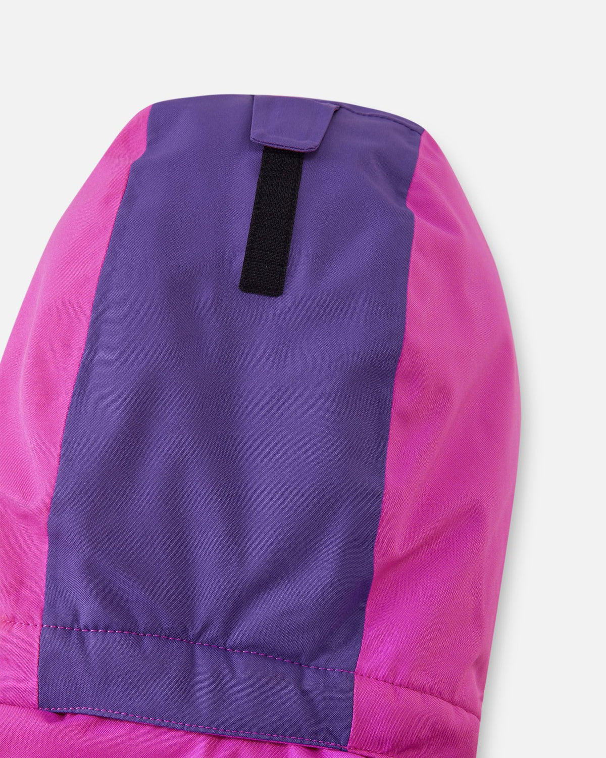 Close-up of the back of the hood on the fuchsia Reima Skaulo girls ski suit, showing the purple color-blocking detail and a velcro strap for easy depth adjustment.