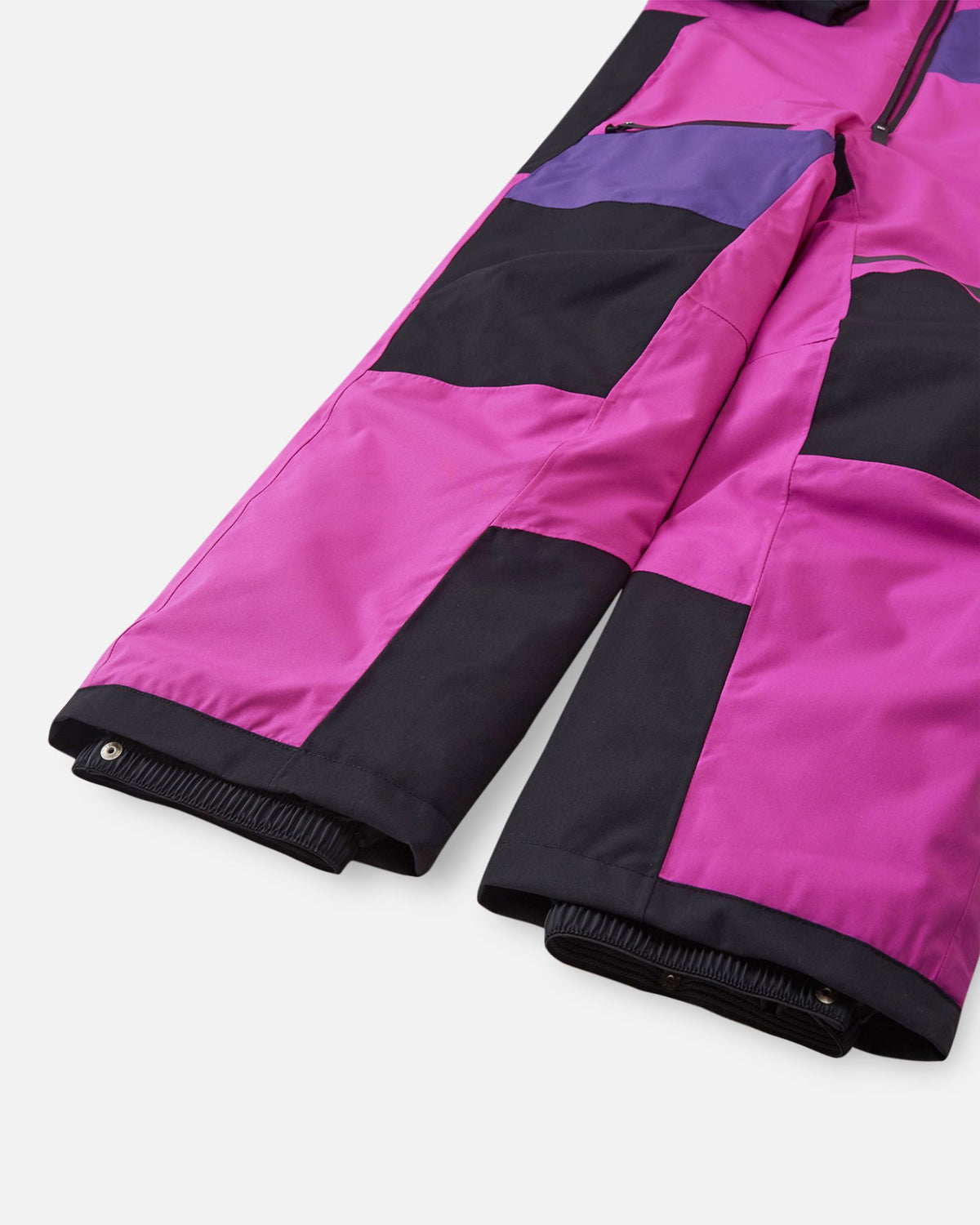 Detail view of the lower legs on the fuchsia Reima Skaulo girls ski suit, displaying the black reinforced knee and hem panels alongside the elastic inner snow locks.