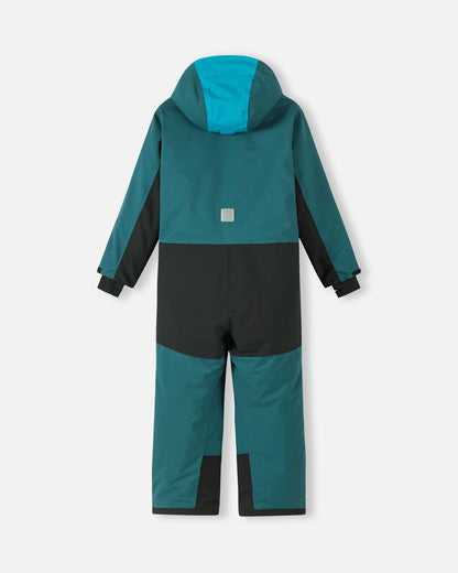Back view of the dark teal Reima Skaulo kids' winter ski suit, highlighting the highly durable black reinforced seat and lower legs, a bright blue hood panel for visibility, and a reflective Reima safety logo on the center back.