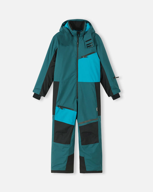 Front view of the Reima Skaulo kids' ski suit in dark teal, featuring bright blue contrast panels, heavy-duty black reinforced knees and inner legs, multiple zippered pockets, and a protective hood designed for winter sports.