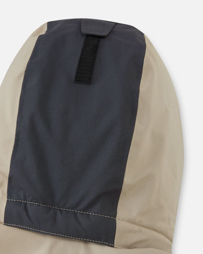 Close-up of the back of the lined, detachable hood on the Reima Skaulo kids ski suit in earthy beige, featuring a velcro adjustment strap for a secure fit.
