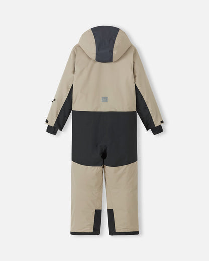 Back view of the Reima Skaulo kids ski suit in earthy beige, showing the durable black reinforcement panels covering the seat and lower legs for active snow play.