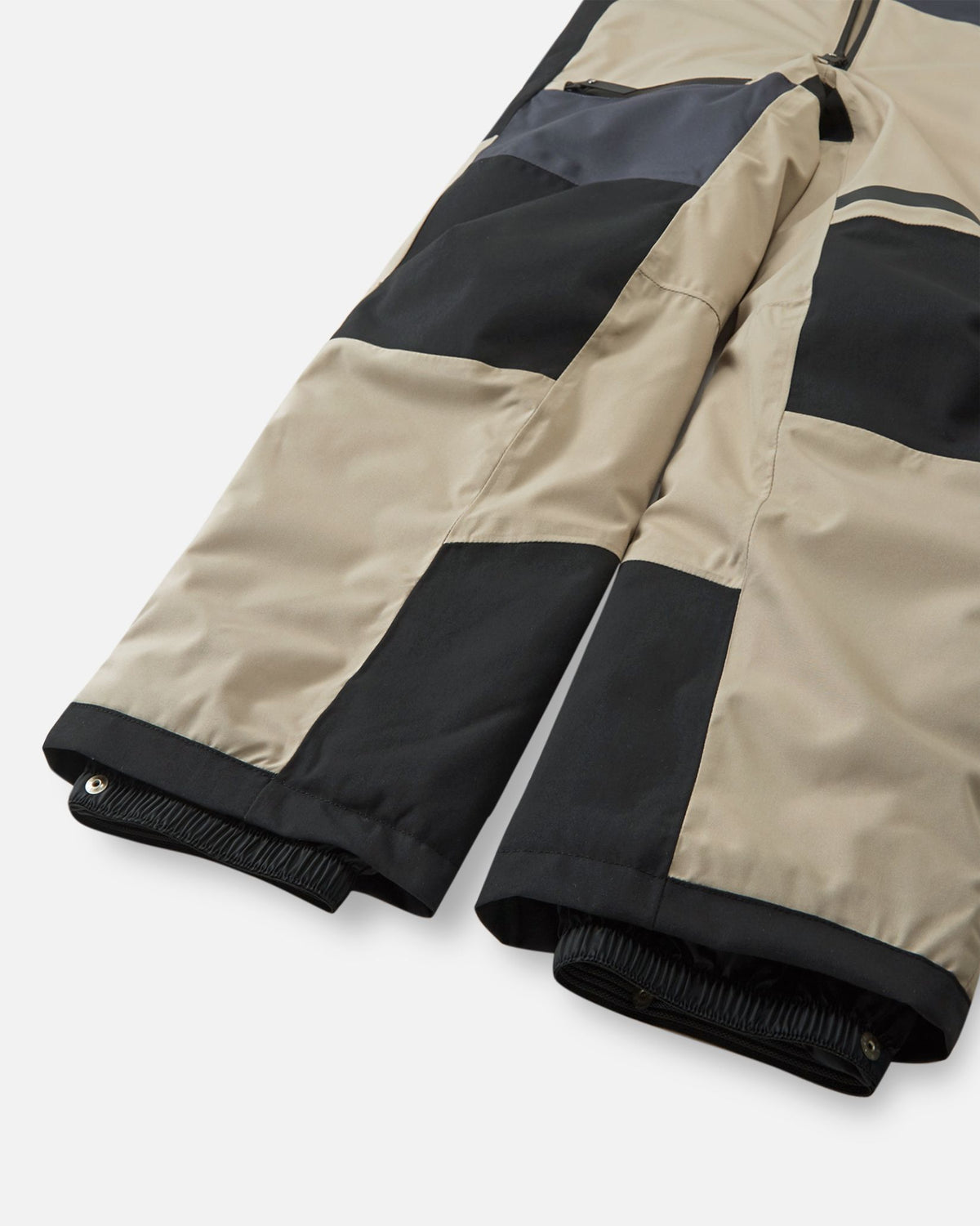 Detail shot of the lower legs on the Reima Skaulo kids ski suit in earthy beige, showing the elastic, adjustable snow locks designed to keep snow out of winter boots.