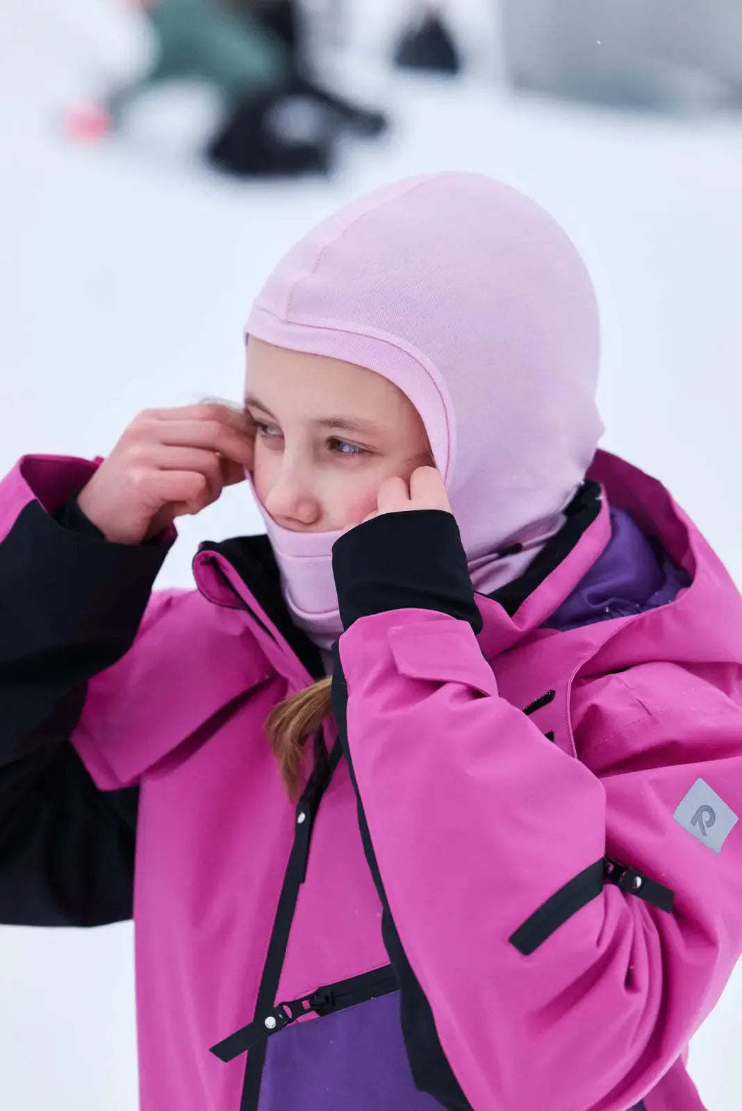 Close-up of a girl wearing the fuchsia Reima Skaulo ski suit, showcasing the jacket's collar and shoulder details in the snow.