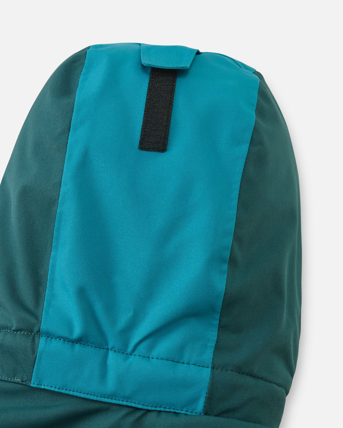Detail shot of the back of the hood on the Reima Skaulo kids' ski suit, showing the practical velcro adjustment strap that allows parents to customize the hood depth for a secure fit over a winter hat or ski helmet.