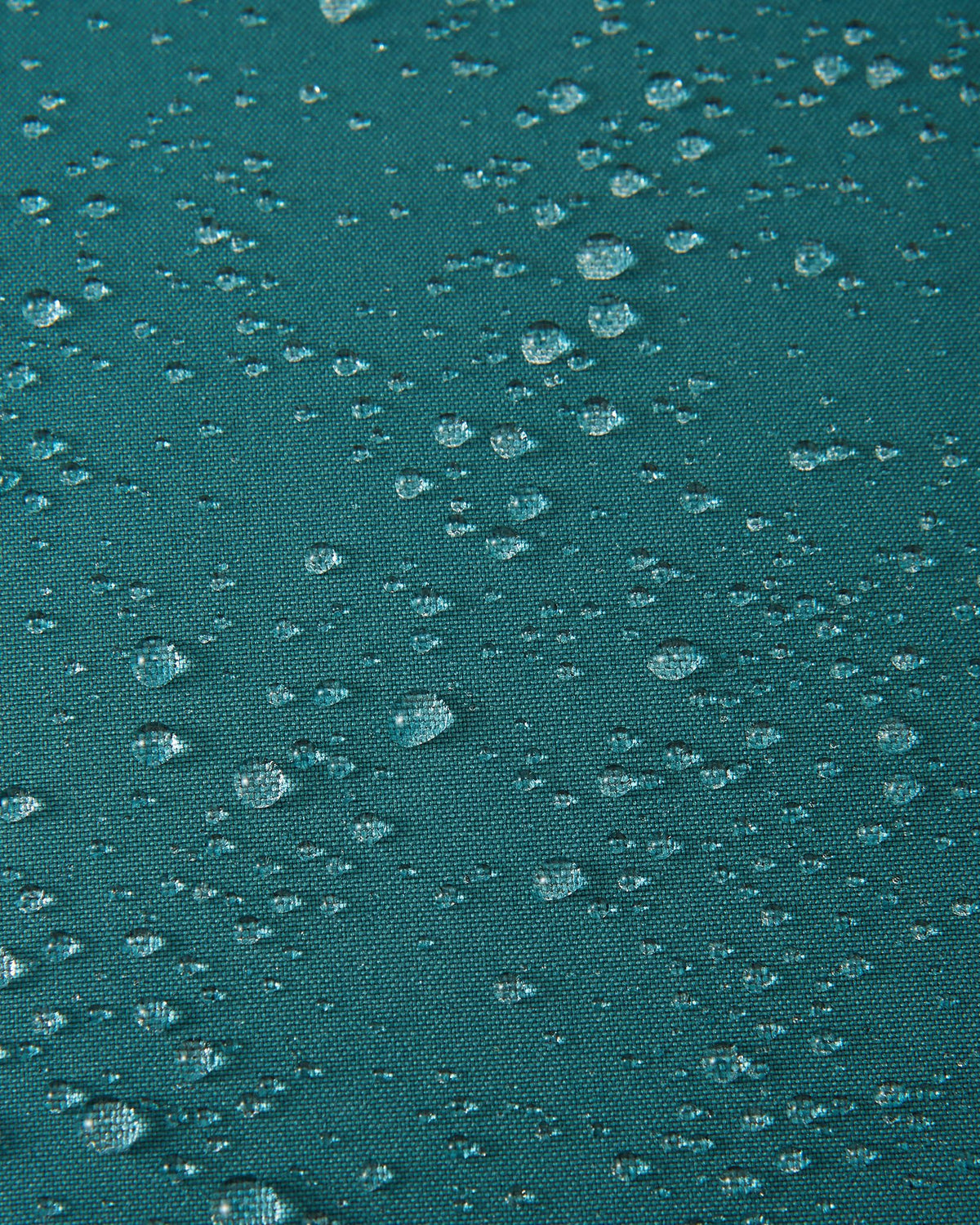 Macro close-up of water droplets tightly beading and resting on the dark teal Reimatec fabric of the Skaulo ski suit, clearly demonstrating the material's advanced waterproof and weather-resistant properties.