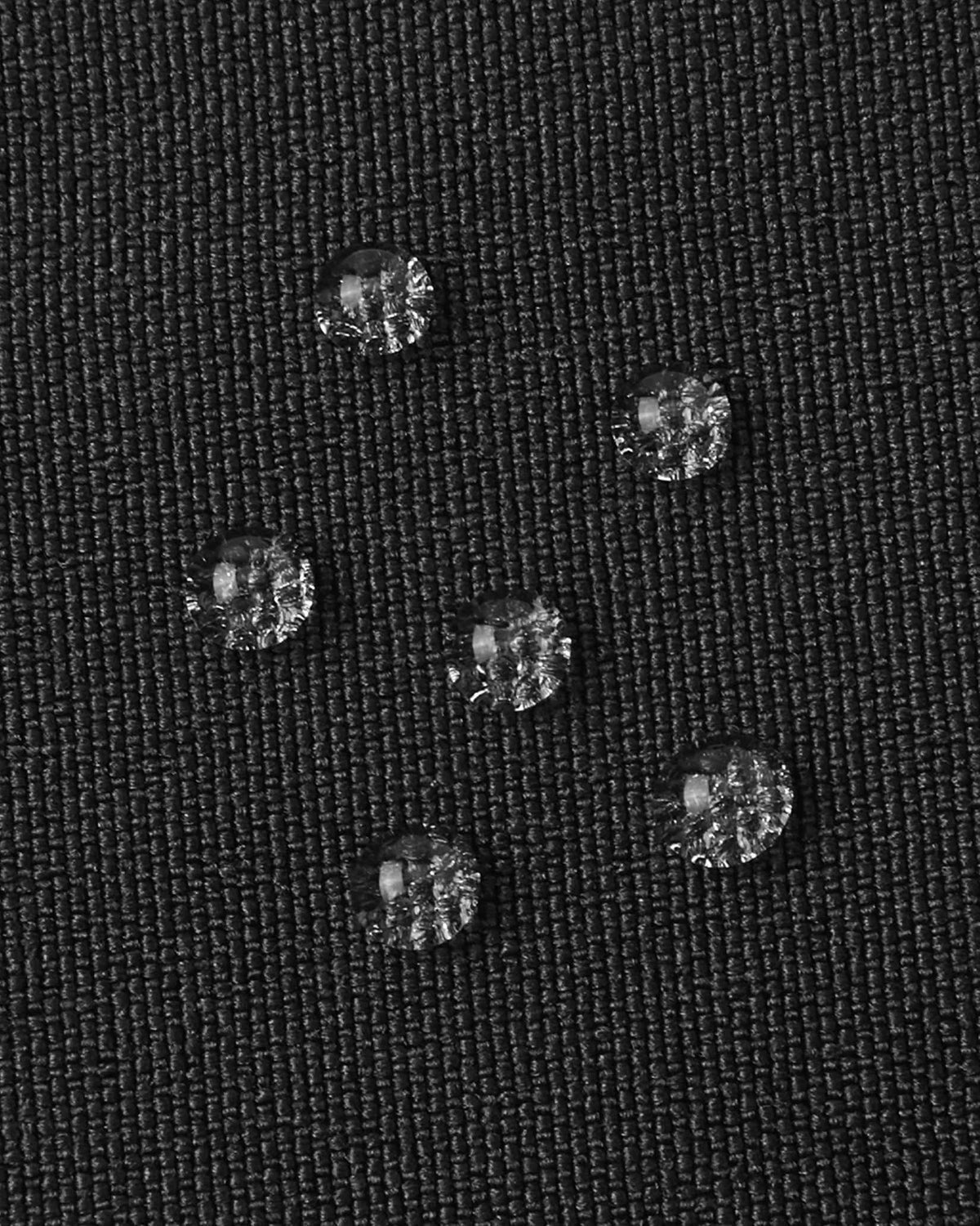 Macro close-up of water droplets actively beading and rolling off the black outer shell of the Reima Skimba kids' ski gloves, demonstrating the high-performance waterproof and breathable technical membrane.