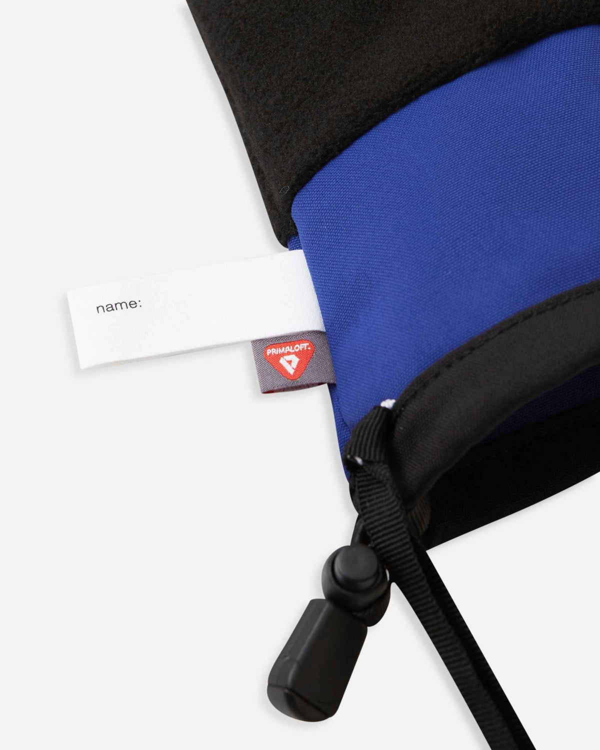 Detail of the inner cuff of the twilight blue Reima Skimba kids' ski gloves, showing the soft black thermal fleece lining, a customizable blank name tag, and the premium PrimaLoft insulation label indicating high-performance winter warmth.