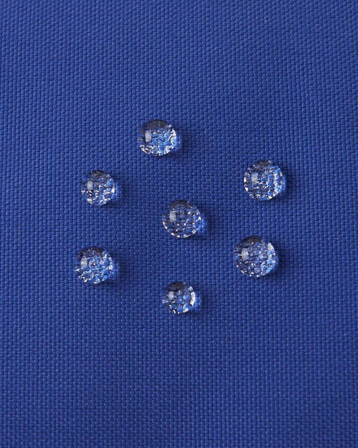 Macro close-up of water droplets actively beading and rolling off the twilight blue outer shell of the Reima Skimba kids' ski gloves, demonstrating the high-performance waterproof and breathable technical membrane.