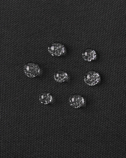 Macro close-up of water droplets actively beading and rolling off the black outer shell of the Reima Snoukka kids' ski mittens, demonstrating the high-performance waterproof and breathable technical membrane.