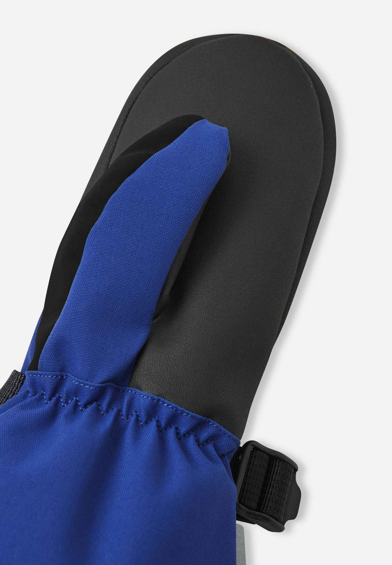 Close-up detail of the black reinforced thumb and palm material on the twilight blue Reima Snoukka kids' ski mittens, engineered for durability and physical dexterity on the slopes.