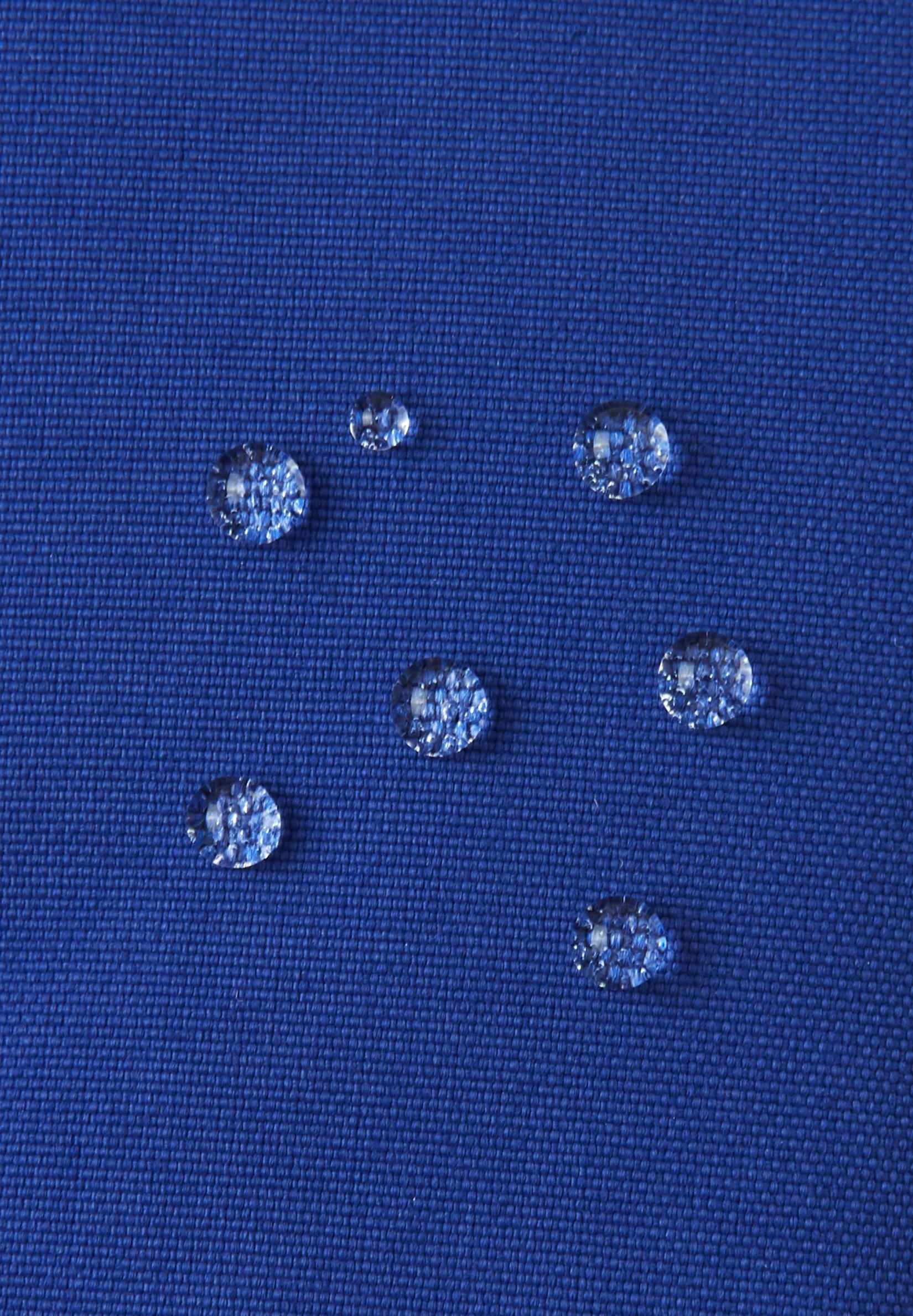 Macro close-up of water droplets actively beading and rolling off the twilight blue outer shell of the Reima Snoukka kids' ski mittens, demonstrating the high-performance waterproof and breathable outer membrane.