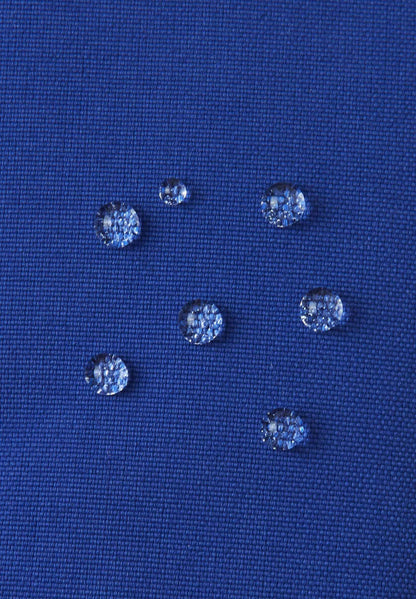 Macro close-up of water droplets actively beading and rolling off the twilight blue outer shell of the Reima Snoukka kids' ski mittens, demonstrating the high-performance waterproof and breathable outer membrane.