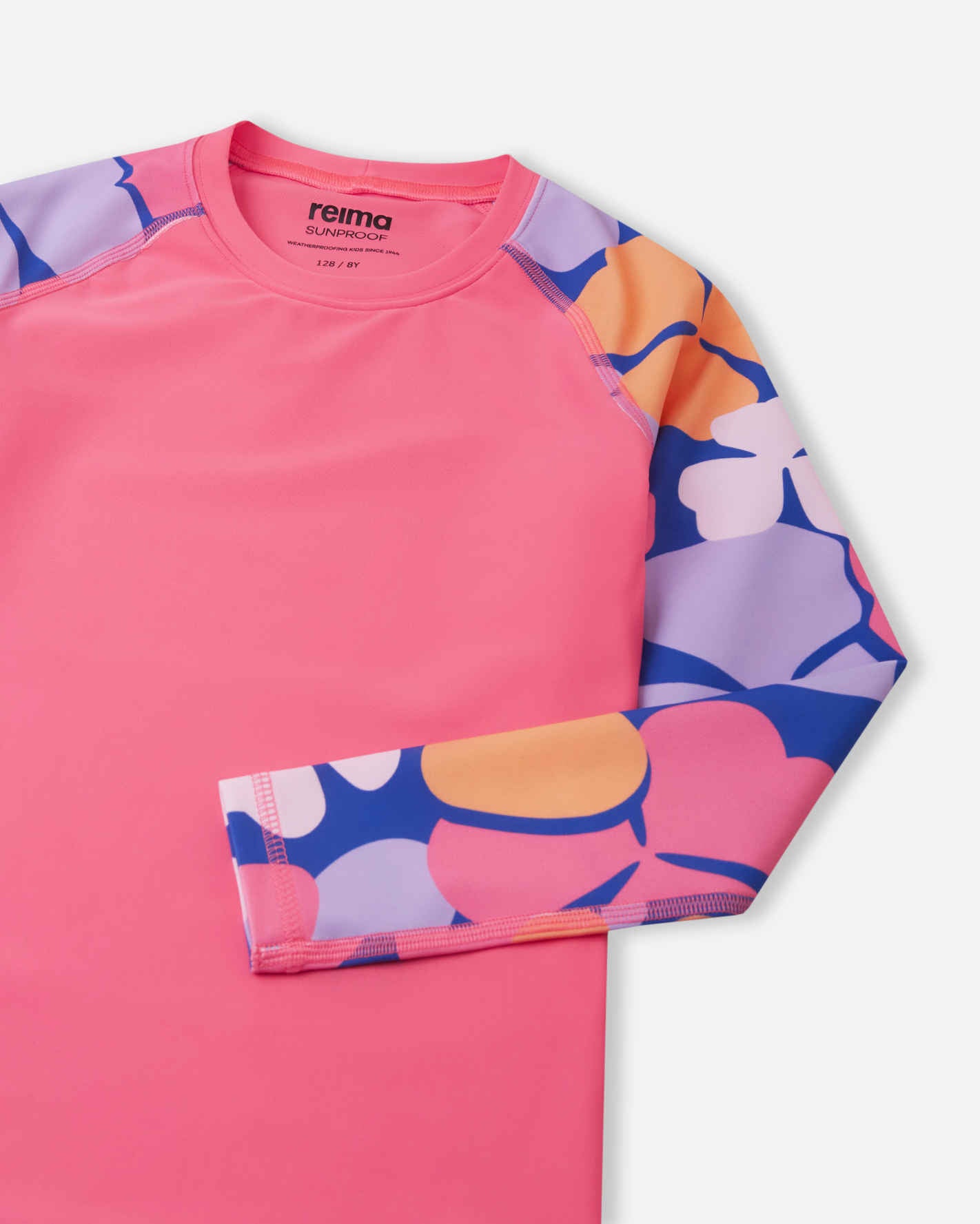 Detailed close-up of the Reima Sukeltaja kids' soft coral sunproof rash guard, focusing on the vibrant floral raglan sleeve, durable anti-chafe seams, and the Reima Sunproof label printed inside the collar.