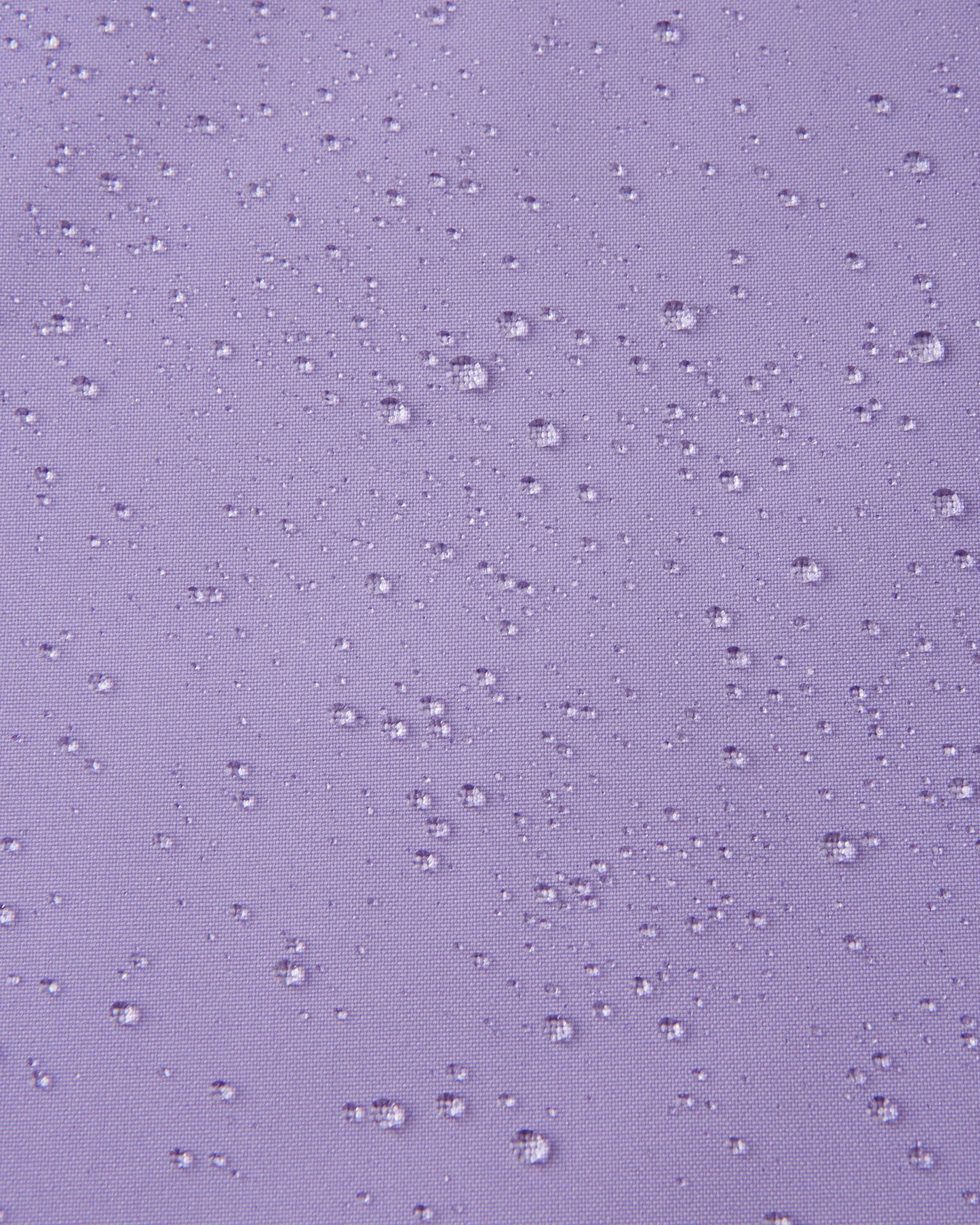 Macro close-up showing water droplets beading tightly on the blooming lilac Reimatec fabric of the Sulkava girls' fall jacket, demonstrating its advanced waterproof and rain-resistant qualities.