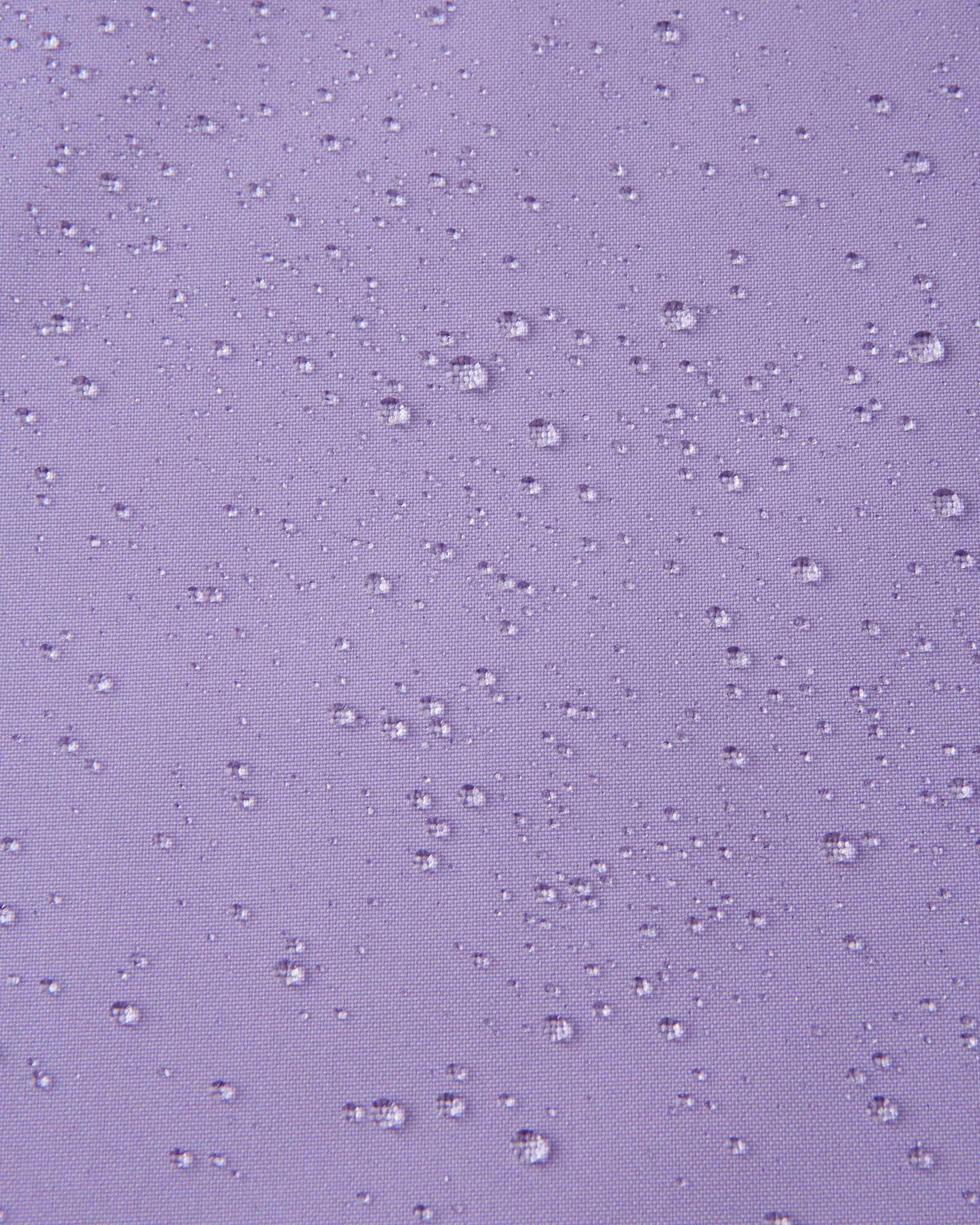 Macro close-up showing water droplets beading tightly on the blooming lilac Reimatec fabric of the Sulkava girls' fall jacket, demonstrating its advanced waterproof and rain-resistant qualities.