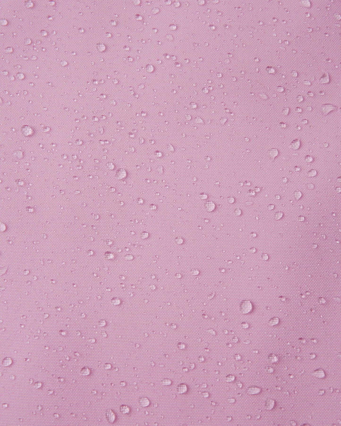 Macro close-up of water droplets tightly beading on the light heather pink Reimatec fabric of the Sulkava girls' fall jacket, demonstrating its advanced waterproof and rain-resistant capabilities for wet weather.