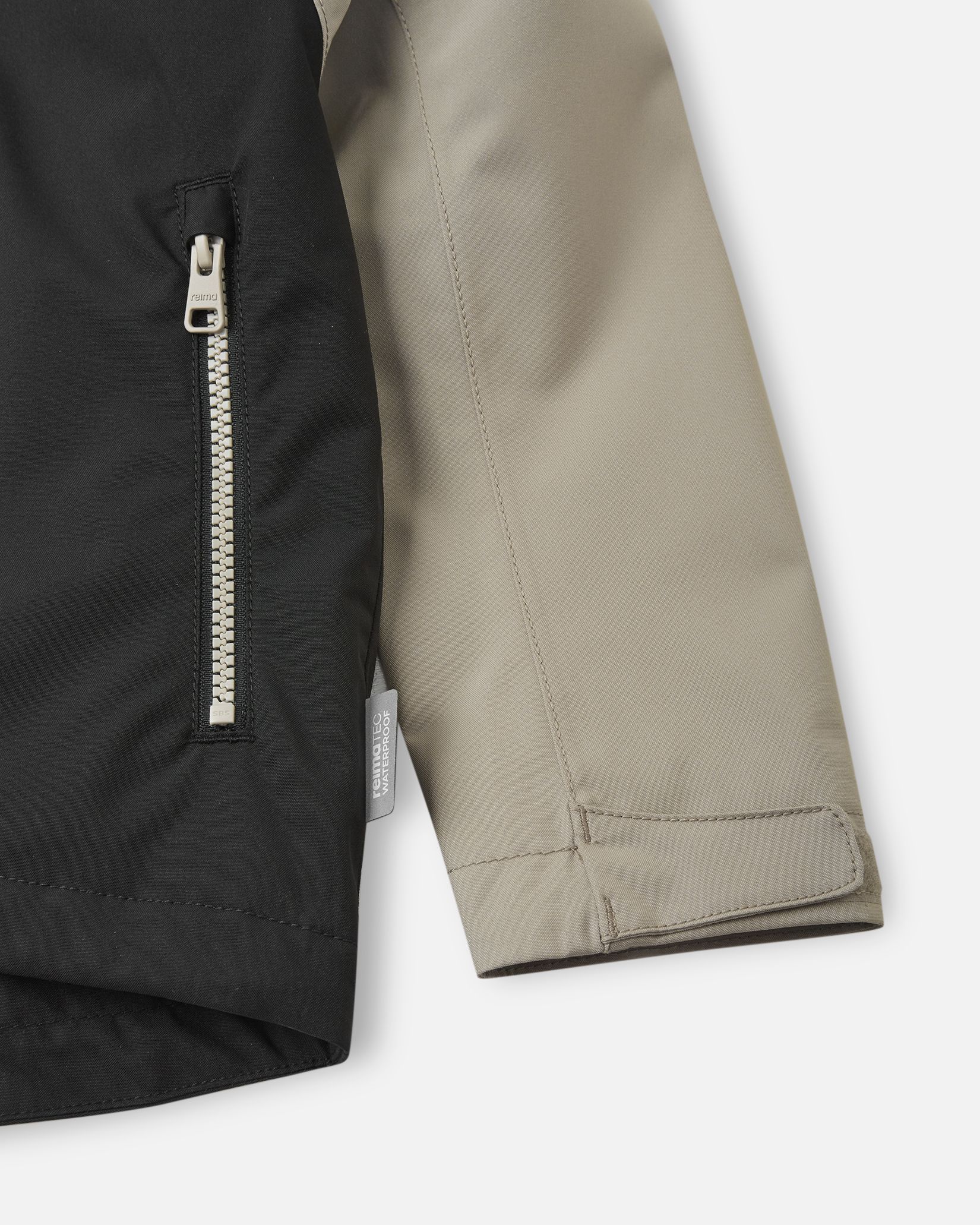Detail shot of the Reima Sulkava jacket showing the contrast between the black body and beige sleeve, featuring a zippered side pocket, a Reimatec waterproof tag, and an adjustable velcro wrist cuff for a secure fit.