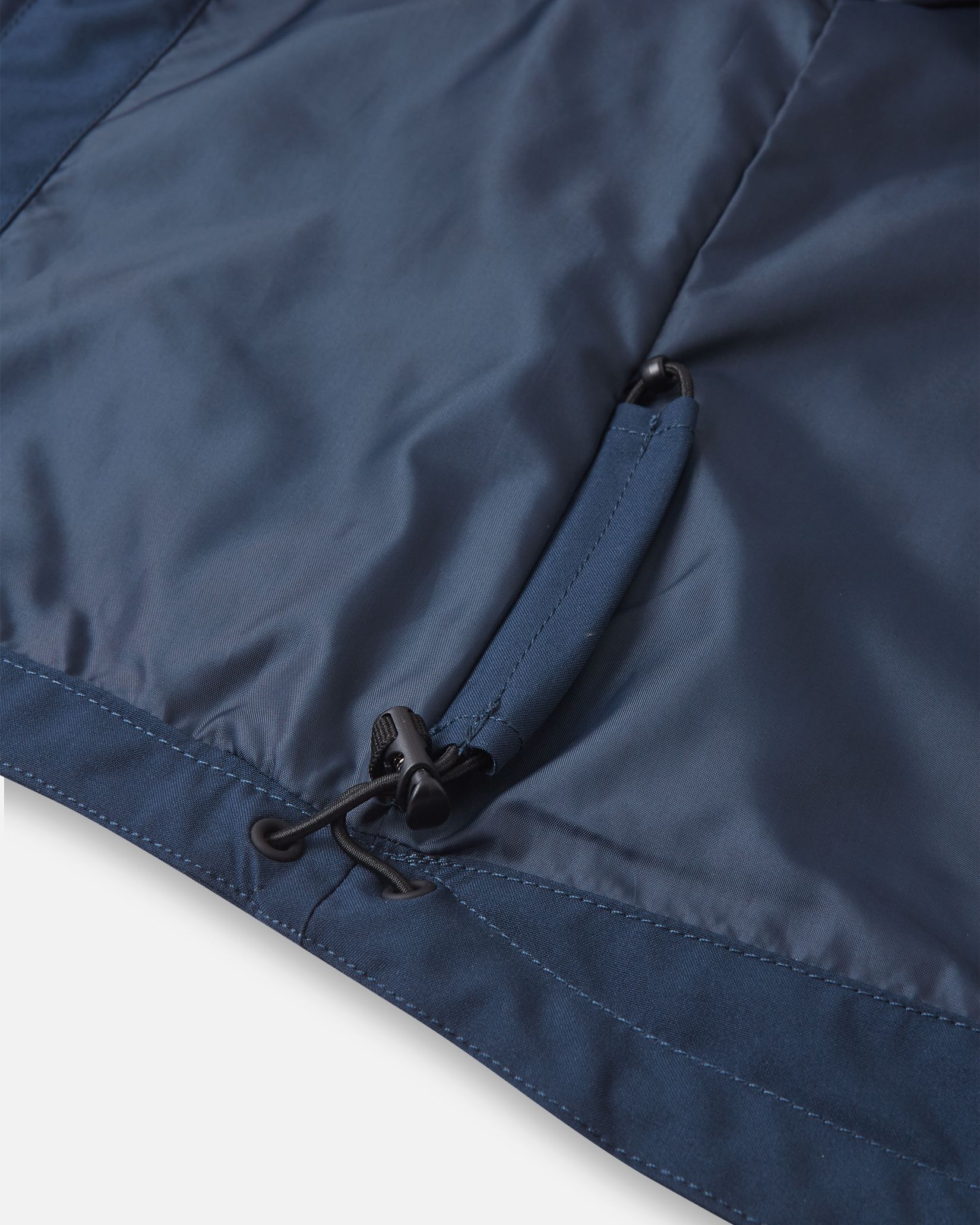 Interior detail shot of the lower hem on the navy blue Reima Sulkava kids' jacket, showcasing the concealed adjustable bungee cord and toggle system used to cinch the hem for a windproof fit.