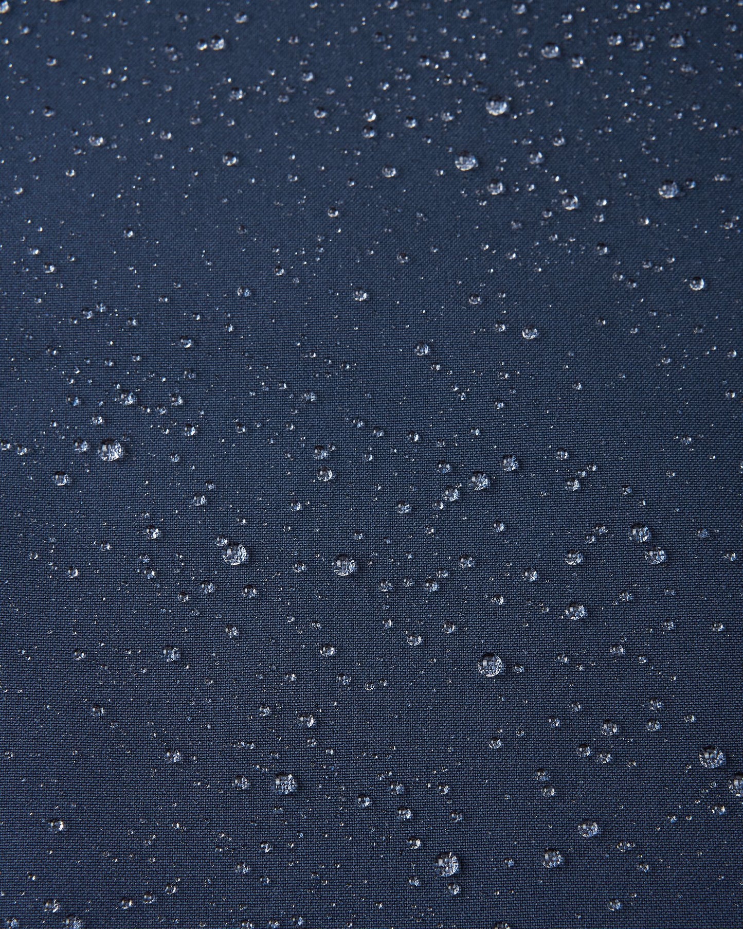 Macro close-up showing water droplets tightly beading on the navy blue Reimatec fabric of the Sulkava kids' fall jacket, demonstrating its advanced waterproof and weather-resistant performance in wet conditions.