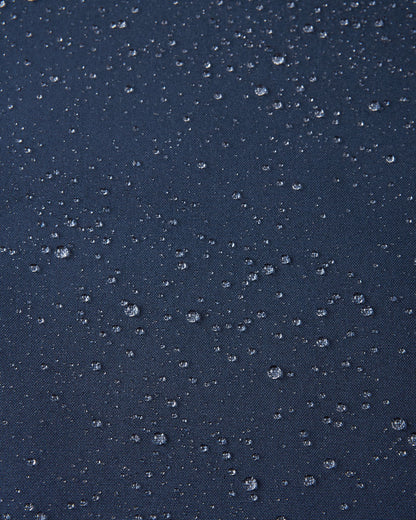 Macro close-up showing water droplets tightly beading on the navy blue Reimatec fabric of the Sulkava kids' fall jacket, demonstrating its advanced waterproof and weather-resistant performance in wet conditions.