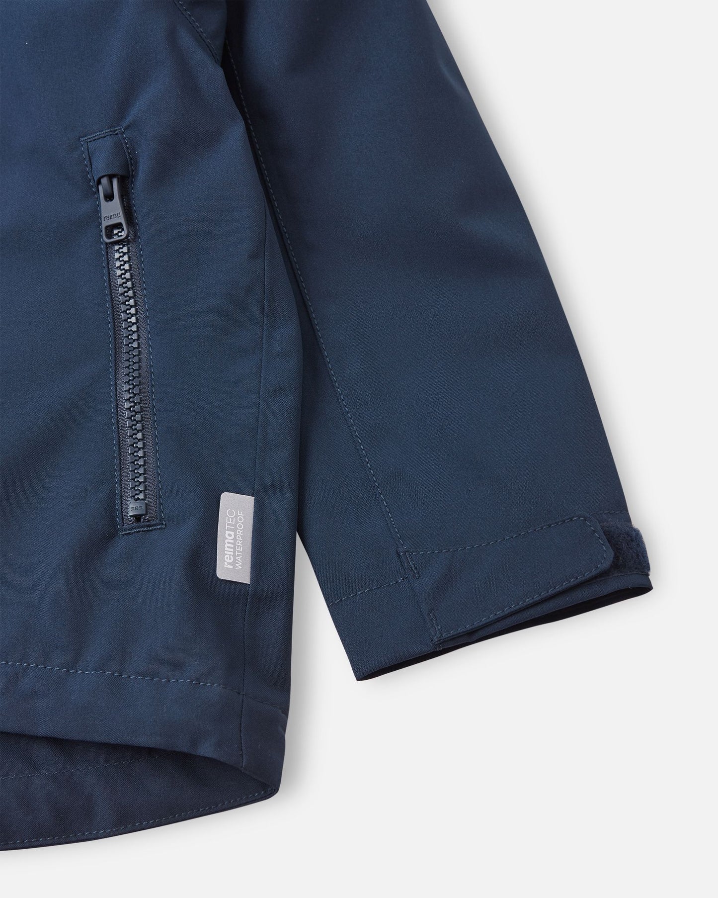 Close-up detail shot of the navy blue Reima Sulkava jacket, highlighting a smooth-running zippered hand pocket, a Reimatec waterproof tag, and an adjustable velcro wrist cuff designed to block out cold drafts.