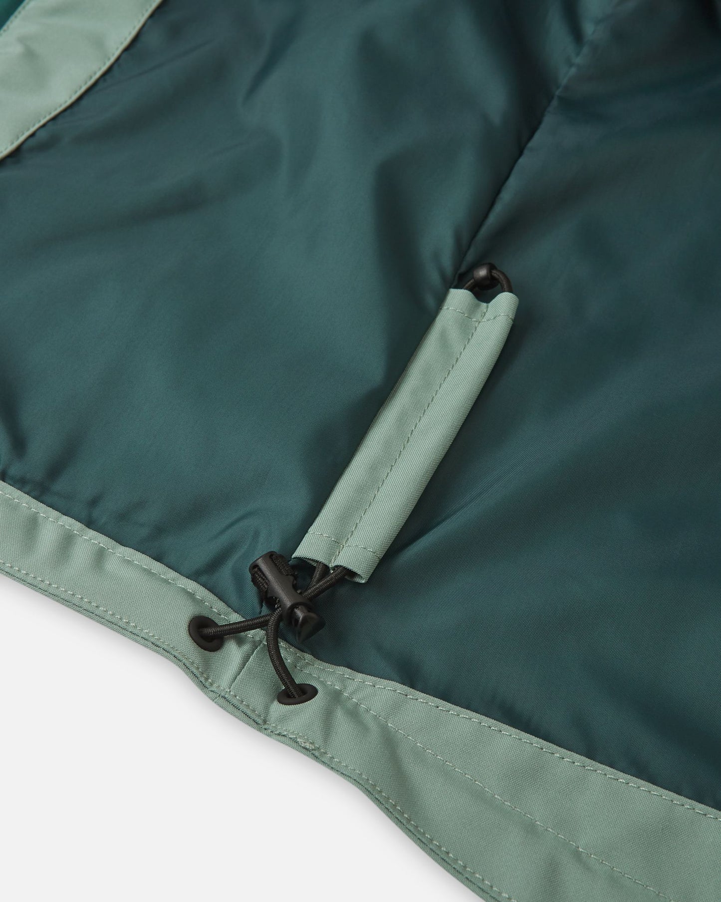 Close-up of the interior lower hem on the Reima Sulkava kids' jacket in stone green, showcasing the concealed, adjustable bungee cord and toggle system designed to cinch the waist and block out cold autumn wind.