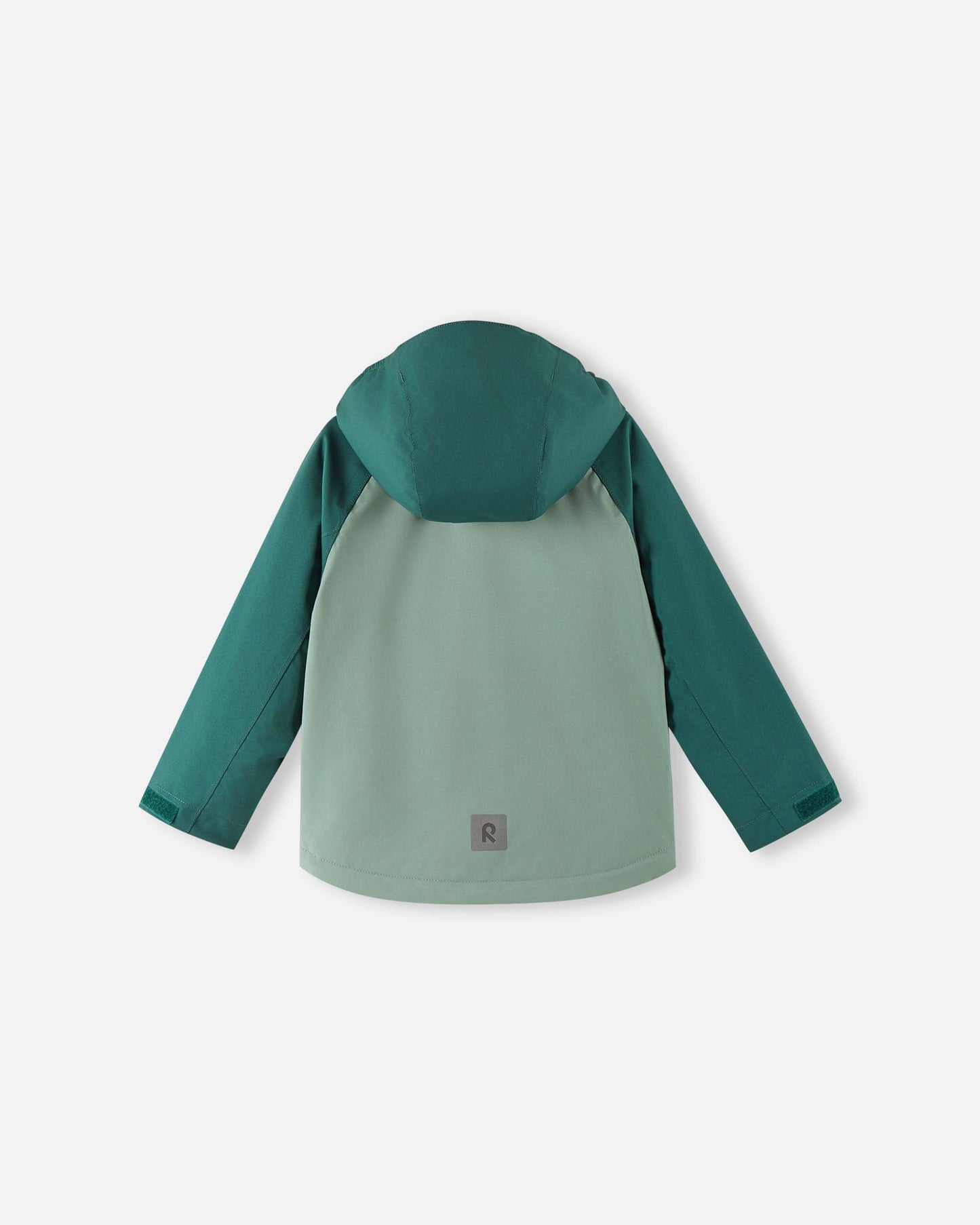 Back view of the Reima Sulkava kids' fall jacket in light and dark stone green, showing the attached hood and a square reflective safety patch positioned near the lower hem for excellent visibility in low light conditions.