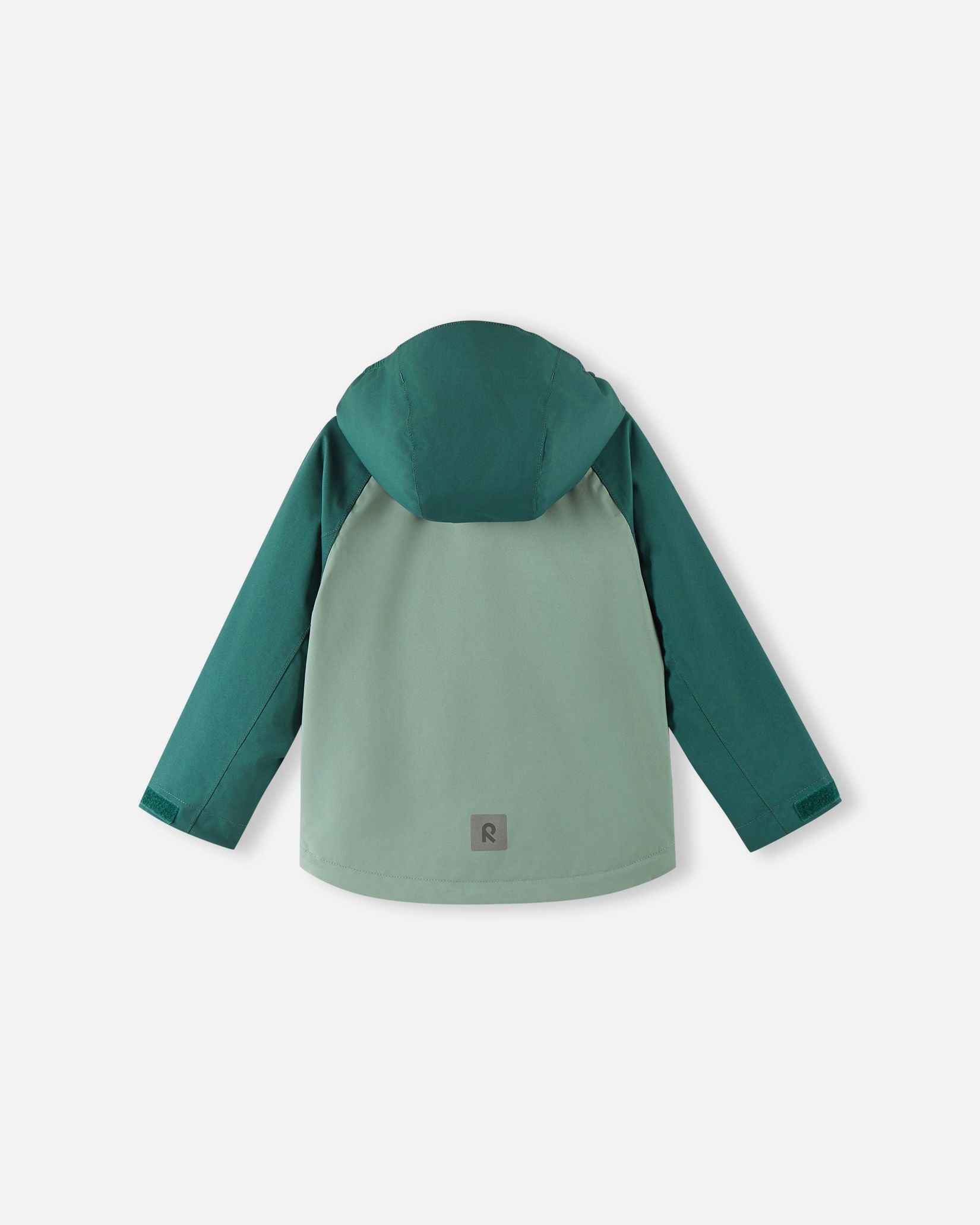 Back view of the Reima Sulkava kids' fall jacket in light and dark stone green, showing the attached hood and a square reflective safety patch positioned near the lower hem for excellent visibility in low light conditions.