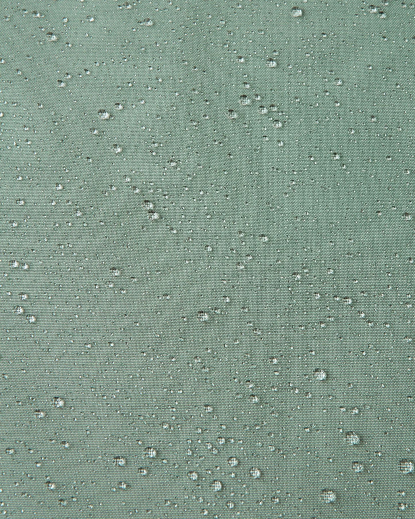Macro close-up demonstrating water droplets tightly beading on the light stone green Reimatec fabric of the Sulkava kids' fall jacket, highlighting its highly effective waterproof and weather-resistant properties.