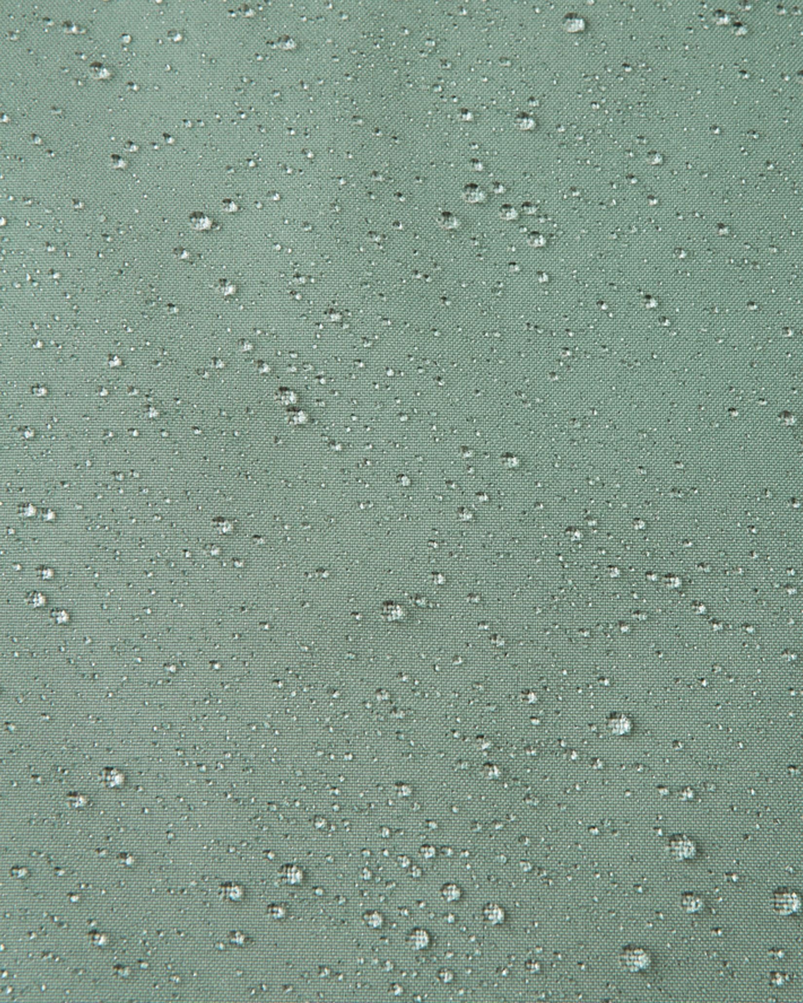 Macro close-up demonstrating water droplets tightly beading on the light stone green Reimatec fabric of the Sulkava kids' fall jacket, highlighting its highly effective waterproof and weather-resistant properties.