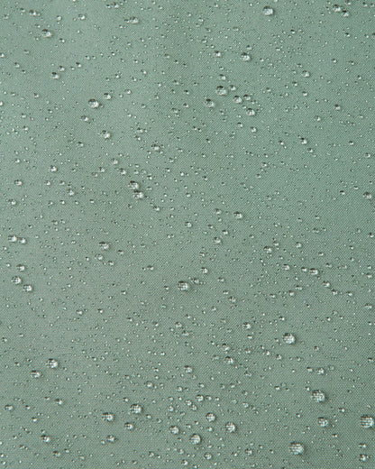 Macro close-up demonstrating water droplets tightly beading on the light stone green Reimatec fabric of the Sulkava kids' fall jacket, highlighting its highly effective waterproof and weather-resistant properties.