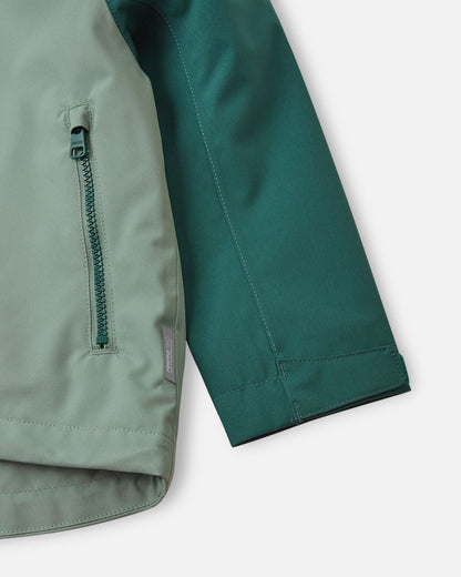 Detail shot of the Reima Sulkava jacket showing the contrast between the light green body and dark stone green sleeve, featuring a zippered side pocket, a Reimatec waterproof tag, and an adjustable velcro wrist cuff for a secure, draft-free fit.