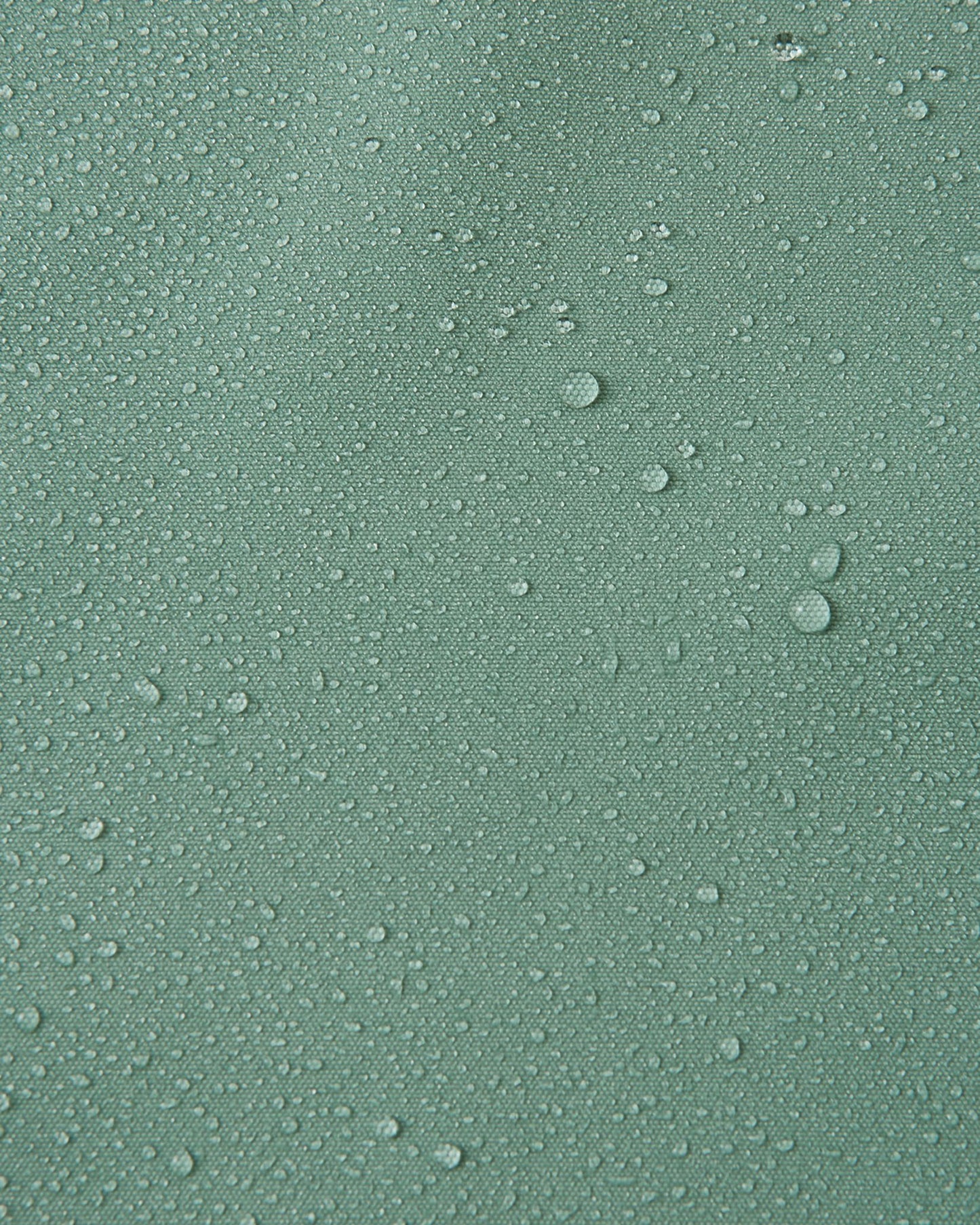 Macro close-up of water droplets beading and rolling off the surface of the Reima Suojala kids' stone green shell jacket, demonstrating its highly waterproof, dirt-repellent Reimatec material.